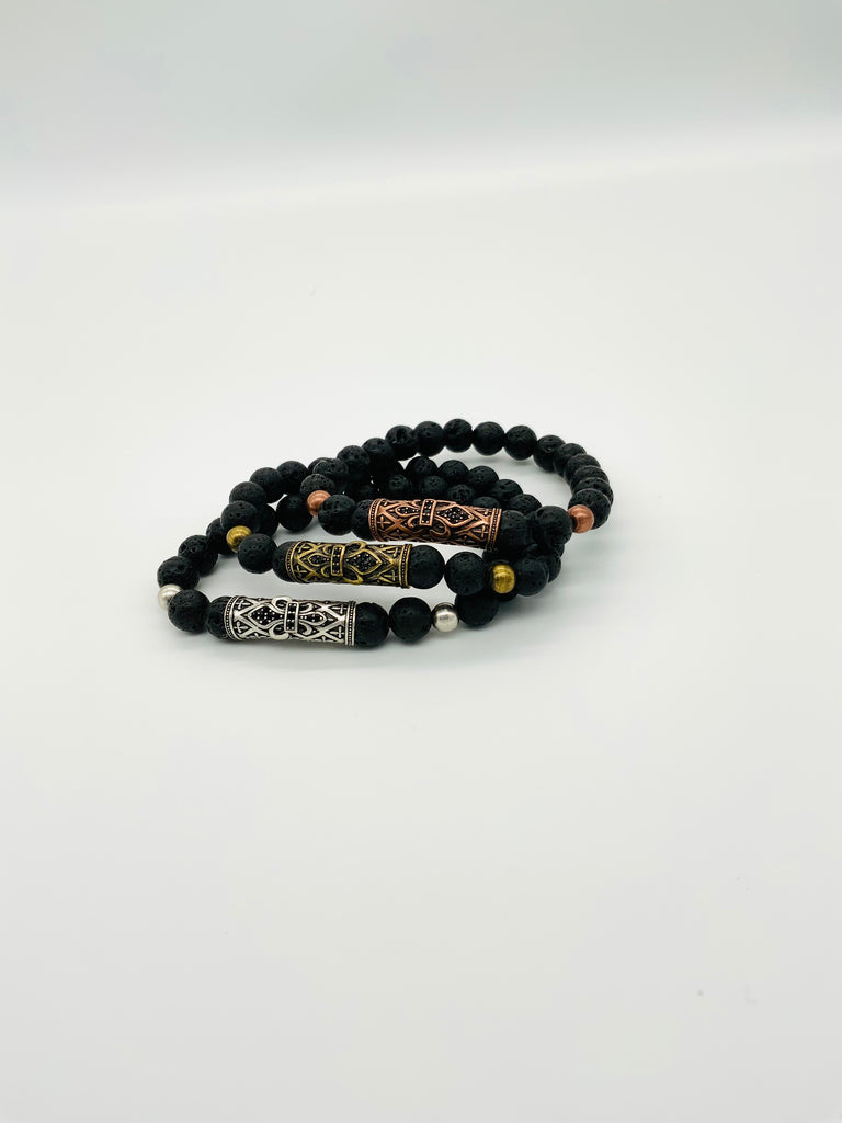 3 stacked black lava rock bracelets with a large accent bead in center. Silver on bottom, gold in the middle, and bronze on top
